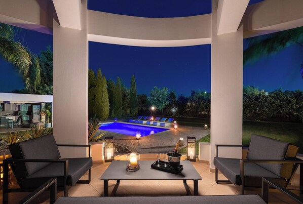 A poolside area with outdoor seating, a table with candles, and a view of a swimming pool at night.