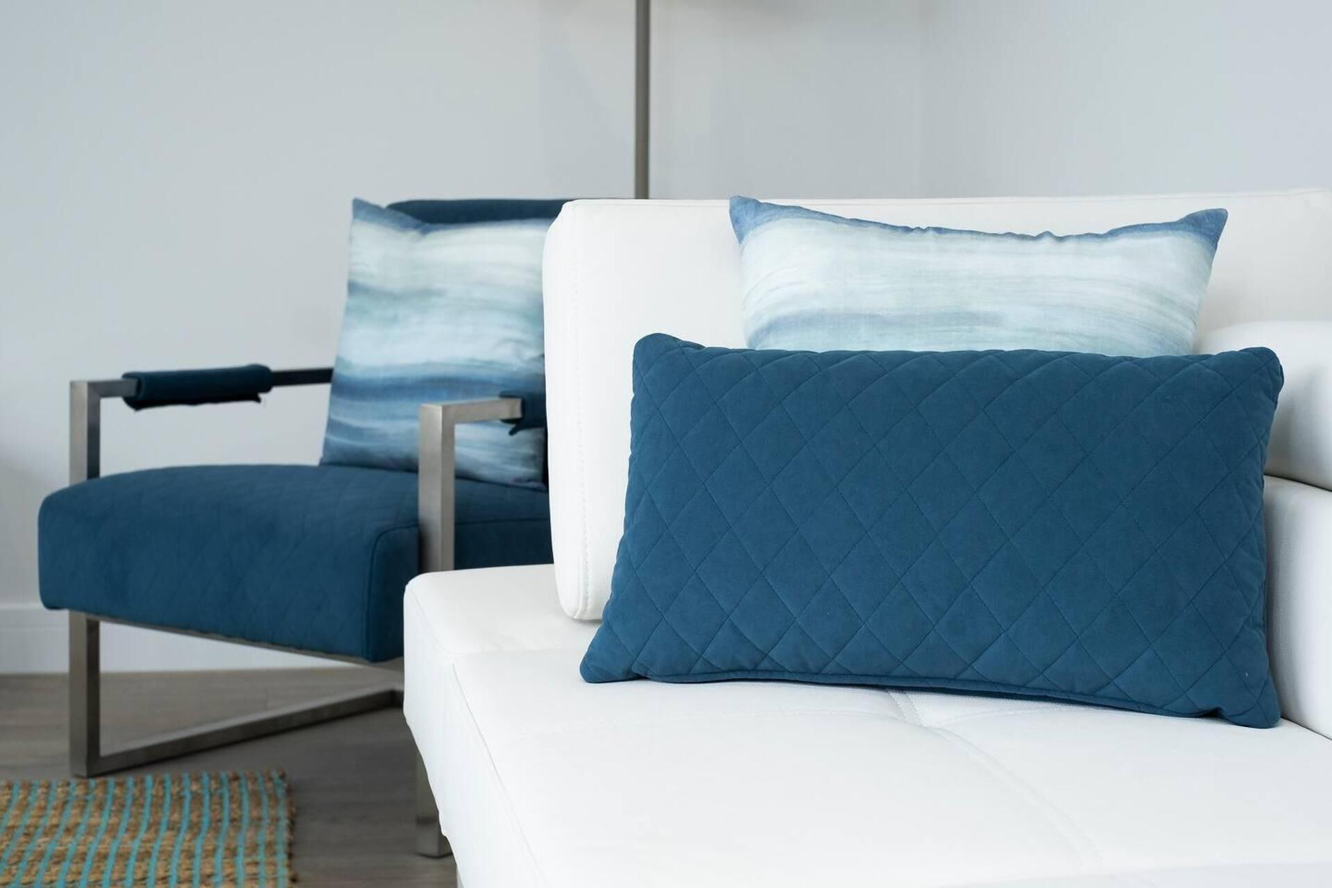 A modern room with a white sofa and a blue armchair, both with matching blue cushions.