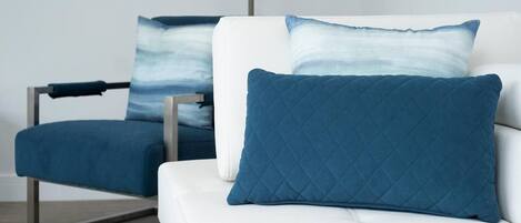 A modern room with a white sofa and a blue armchair, both with matching blue cushions.