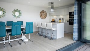 A modern kitchen with white cabinets, a central island with bar stools, and a large clock on the wall. - This Apartment is No Longer Available (Woolacombe)