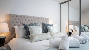 A neatly made bed with a tufted headboard, multiple pillows, and a set of towels. - This Apartment is No Longer Available (Woolacombe)