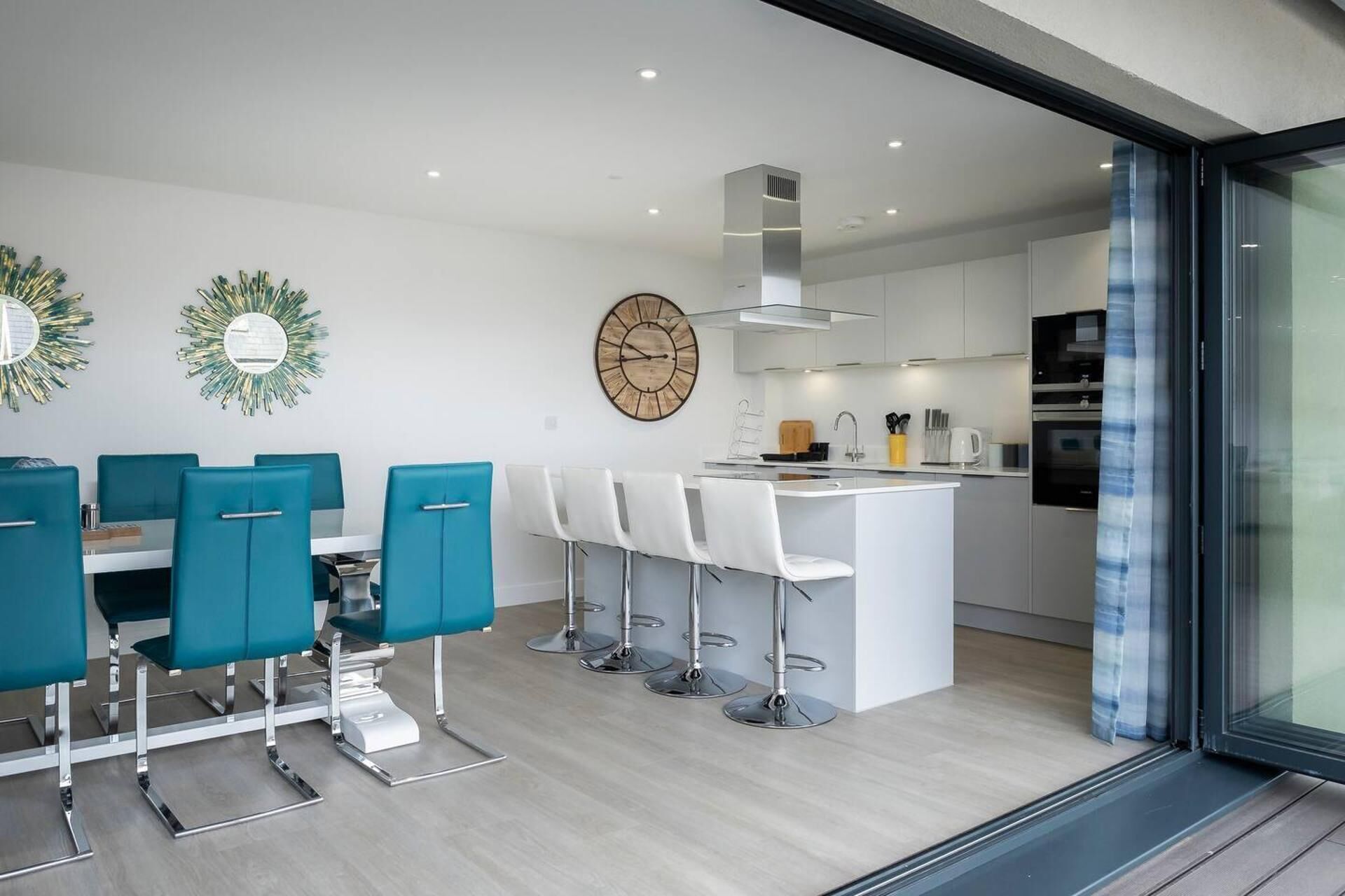 Una cocina moderna con armarios blancos, una isla central con taburetes y un reloj grande en la pared.