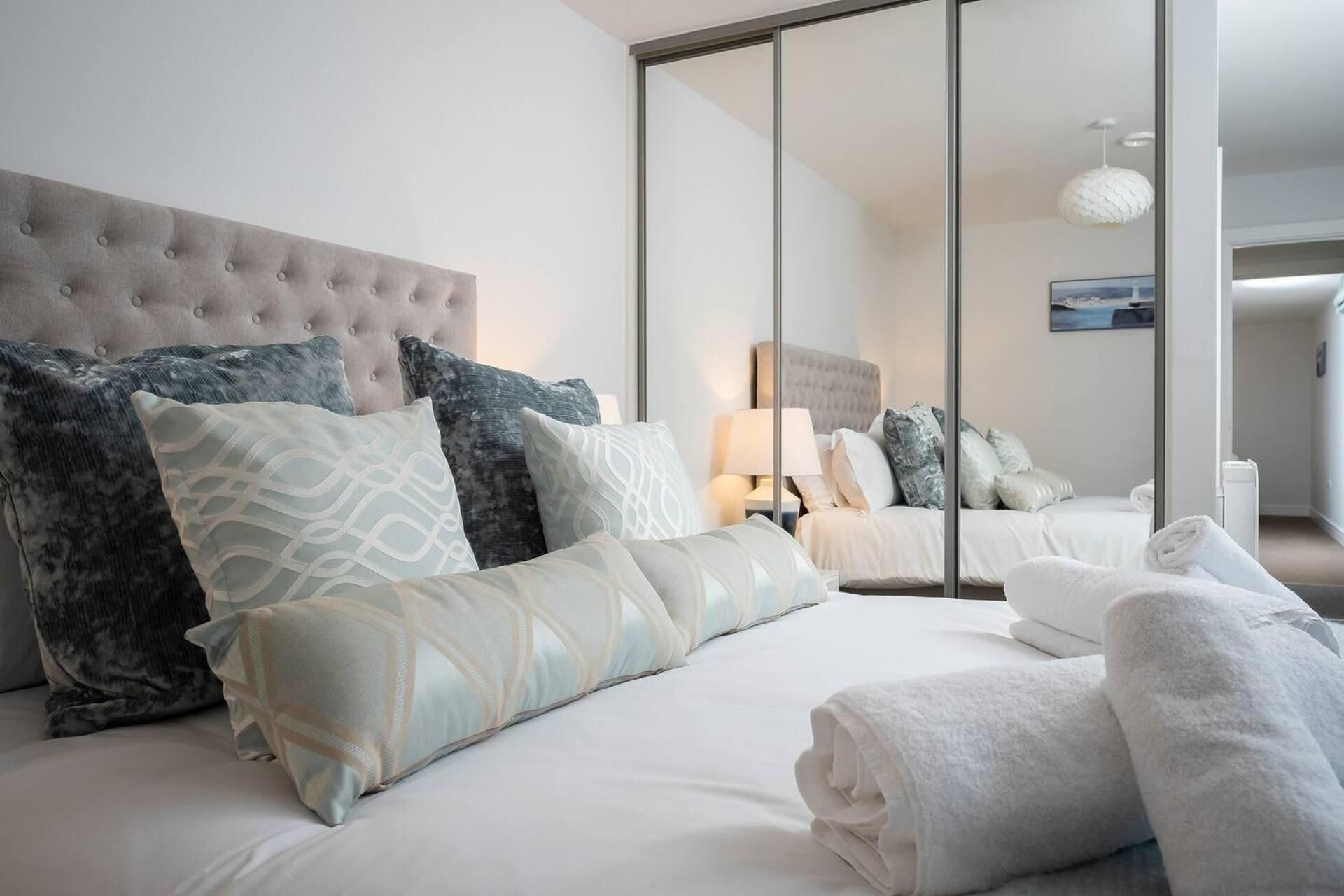 Ett modernt hotellrum med en stor säng, flera kuddar, ett sängbord med en lampa och utsikt genom en skjutdörr.