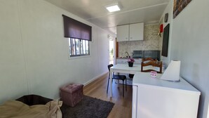 A compact kitchen with a dining area, a small seating space, and a window with blinds. - CHALET DESIGN NATURA JACUZZI GUEST DREAM (Esposende)