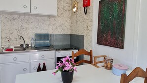 A compact kitchen with white cabinets, a stove, and a sink. There's a clock on the wall and a painting above the counter. - CHALET DESIGN NATURA JACUZZI GUEST DREAM (Esposende)