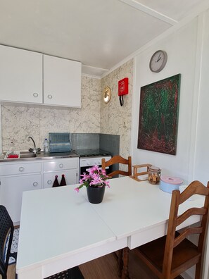 A compact kitchen with white cabinets, a stove, and a sink. There's a clock on the wall and a painting above the counter.
