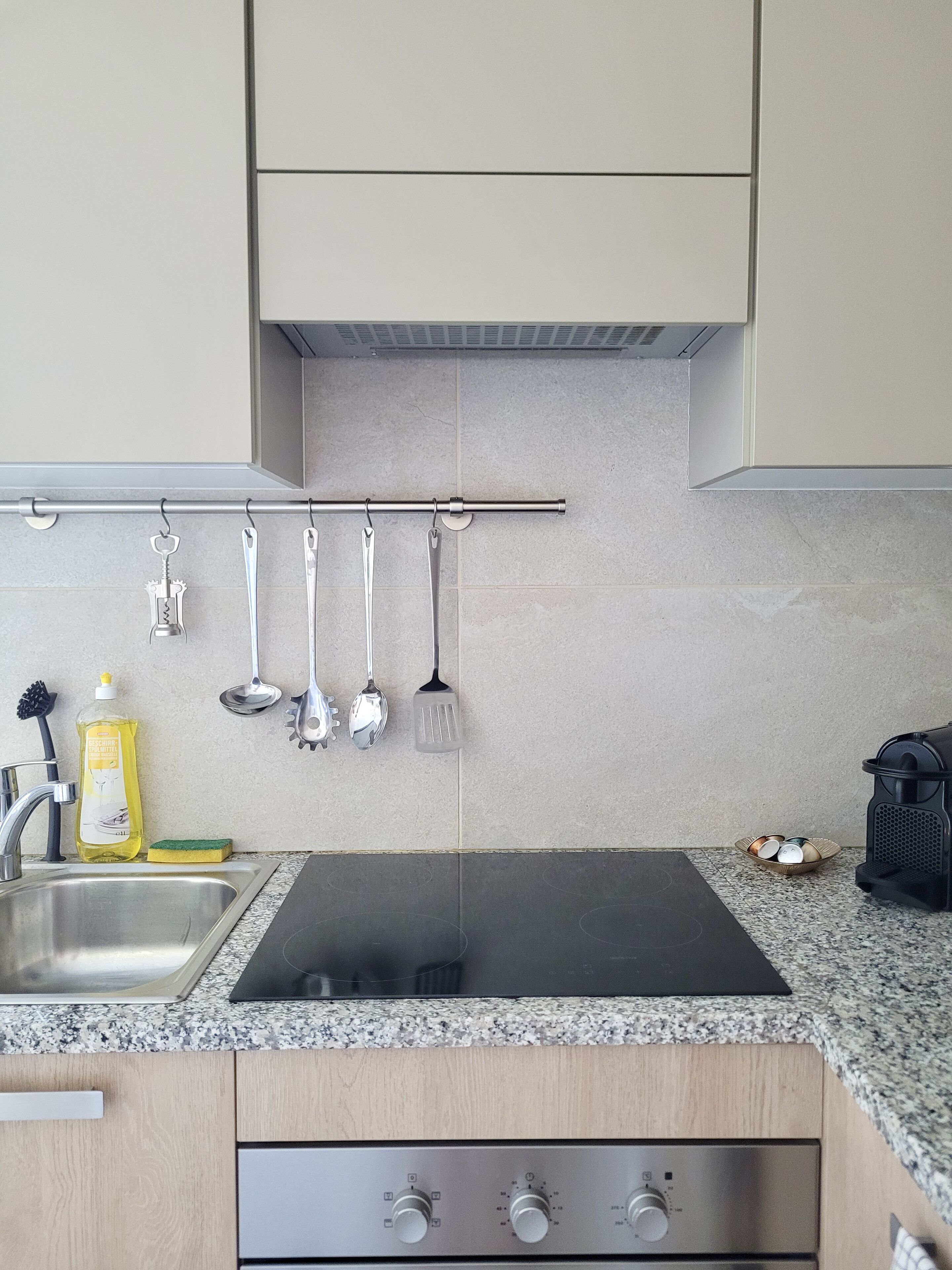 Een keuken met een roestvrijstalen spoelbak, een zwart fornuis en houten kastjes.