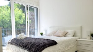 A modern bedroom with a large bed, a bedside table, a chair, and a view of greenery through a sliding glass door. - Central and cozy- FREE PARKING (Lugano)