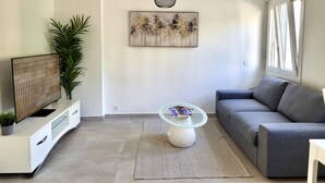 A modern living room with a grey sofa, a glass coffee table, a TV on a white cabinet, and a large plant. - Central and cozy- FREE PARKING (Lugano)