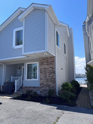 A two-story house with a porch, brick foundation, and a view of the water.