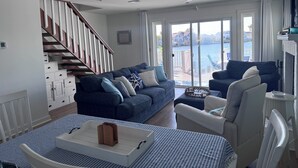 Een moderne woonkamer met een trap, een zithoek, een eettafel en uitzicht op het water.