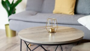A round wooden coffee table with a gold geometric base, placed on a textured rug.