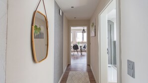 A hallway with a wooden floor, a white rug, a mirror, and a dining area with chairs and a table in the background.
