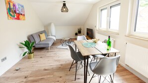 A modern living room with a dining area, a grey sofa, a wooden dining table, and a TV on the wall.