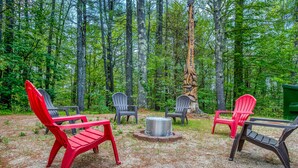 A forest setting with outdoor seating including red and gray Adirondack chairs around a central fire pit. - Expansive lodge| 9 Br | Indoor Pool | Sauna | Game Room | 3 Bath (Conway)
