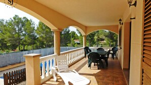 A covered outdoor patio with a white lounge chair, a table with chairs, and a view of trees and a fence. - Pleasant villa with pool (A) (Ametlla de Mar (Les Tres Cales))