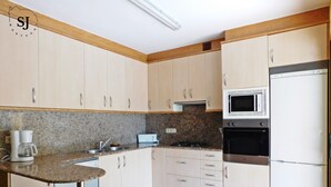 A kitchen with light-colored cabinets, a microwave, an oven, a coffee maker, and a small bar stool. - Pleasant villa with pool (A) (Ametlla de Mar (Les Tres Cales))