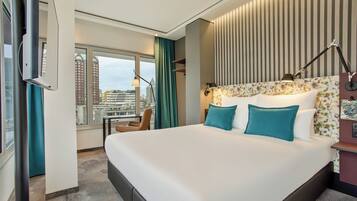 Habitación de hotel moderna con una cama grande, vista a la ciudad y paisaje urbano visible a través de la ventana.