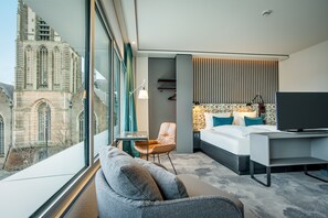 A modern hotel room with a large window, a bed, a desk, and a chair.