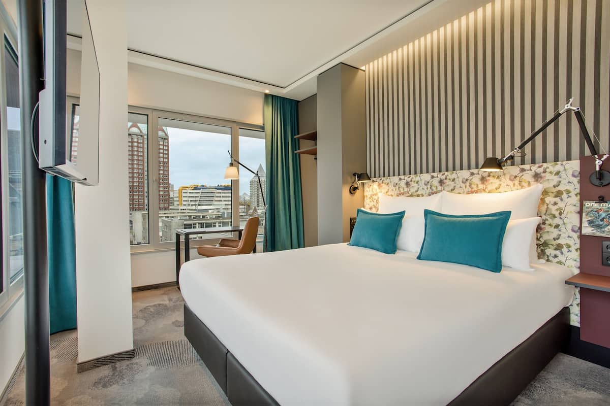 Una habitación de hotel moderna con una cama grande, vistas de la ciudad y un escritorio con una silla.
