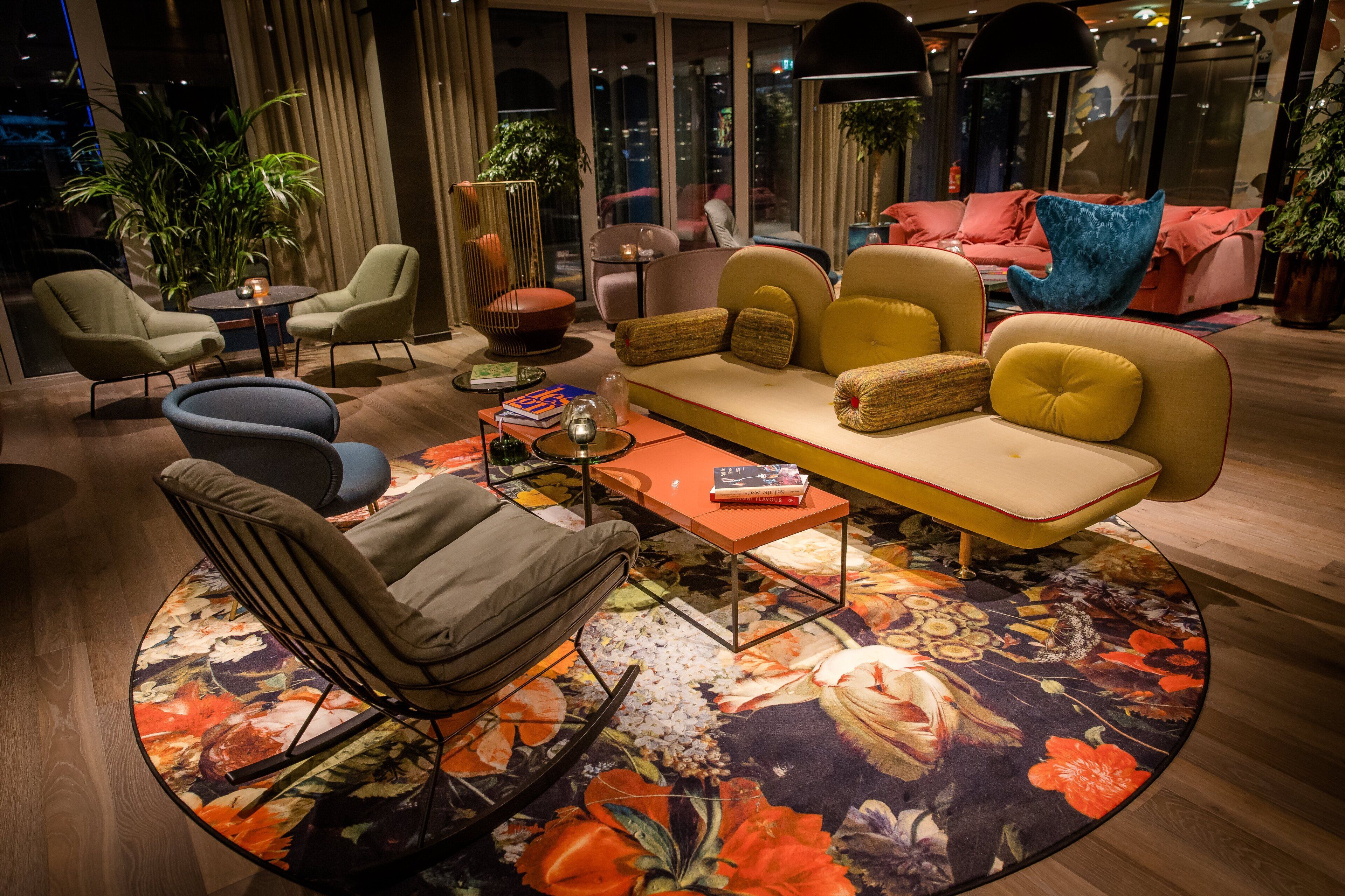 A modern living room with a sofa, chairs, and a coffee table. There are plants and a large window in the background.