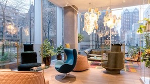 A modern interior with large windows, a black chair, a blue chair, and a patterned rug.