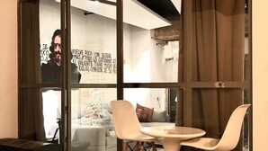 Un comedor moderno con una mesa redonda y dos sillas, ventanas amplias con cortinas, y una cocina visible al fondo.