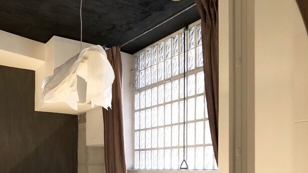Un dormitorio con cama, una silla, lámpara colgante y ventana con cortinas.