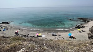 Une plage avec une eau turquoise et limpide, un rivage rocheux et plusieurs parasols.