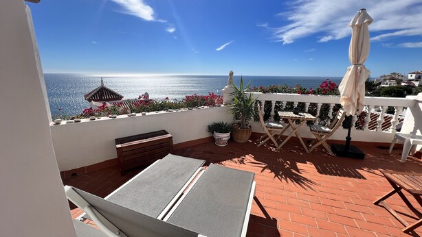 Un balcon avec vue sur la mer, une table avec des chaises, un banc et un pot de fleurs.