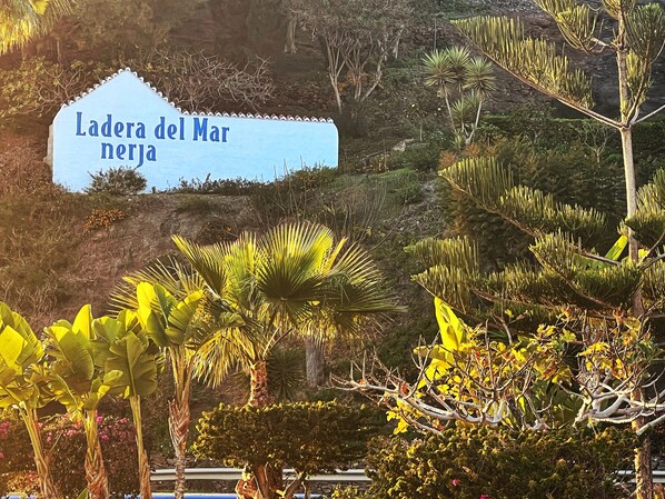 A sign reading "Ladera del Mar nerja" amidst a lush garden with various tropical plants. - Spectacular panoramic sea view in Nerja. Sun from sunrise to sunset. (AN)