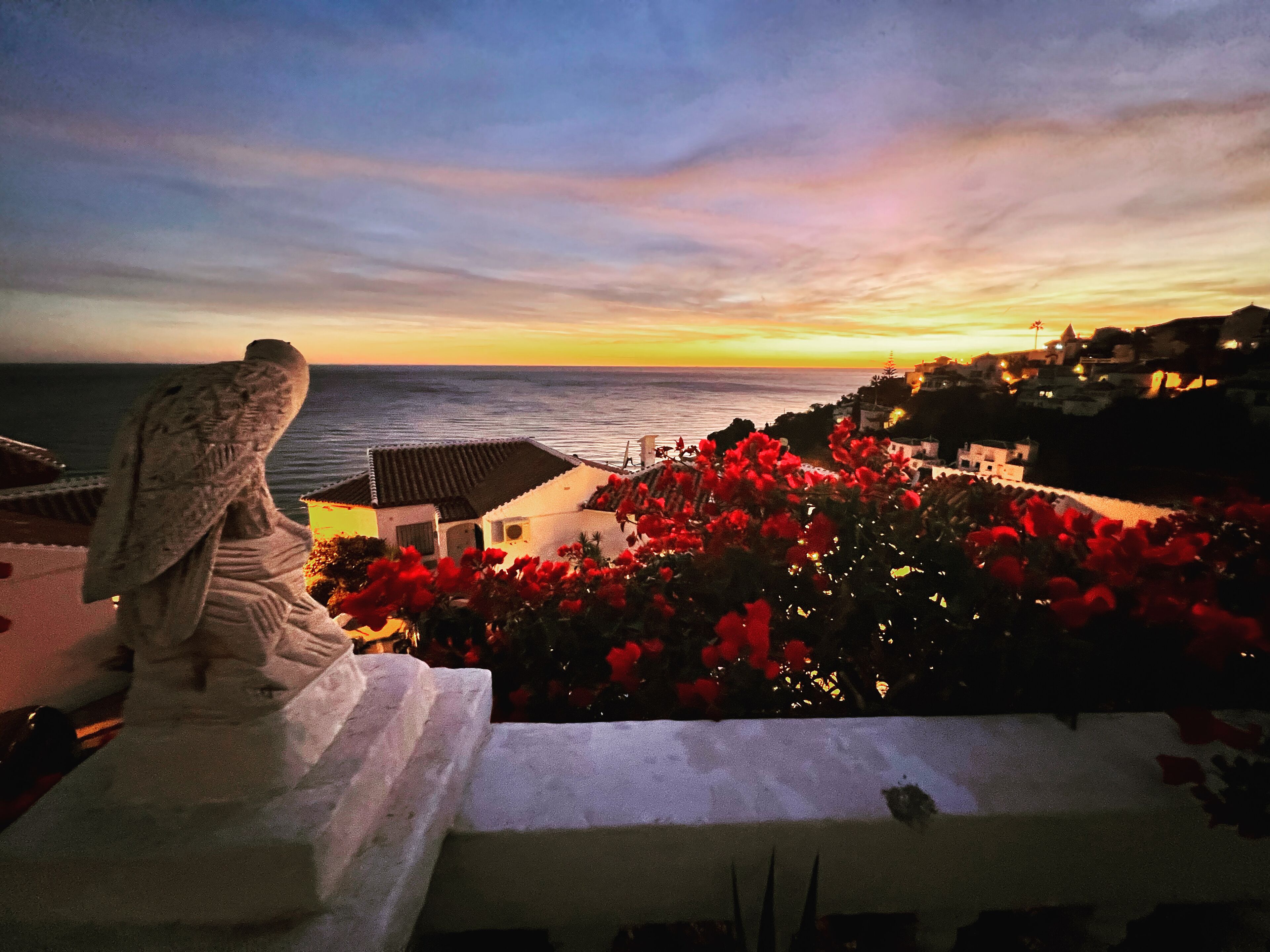 A statue overlooking a coastal town at sunset.