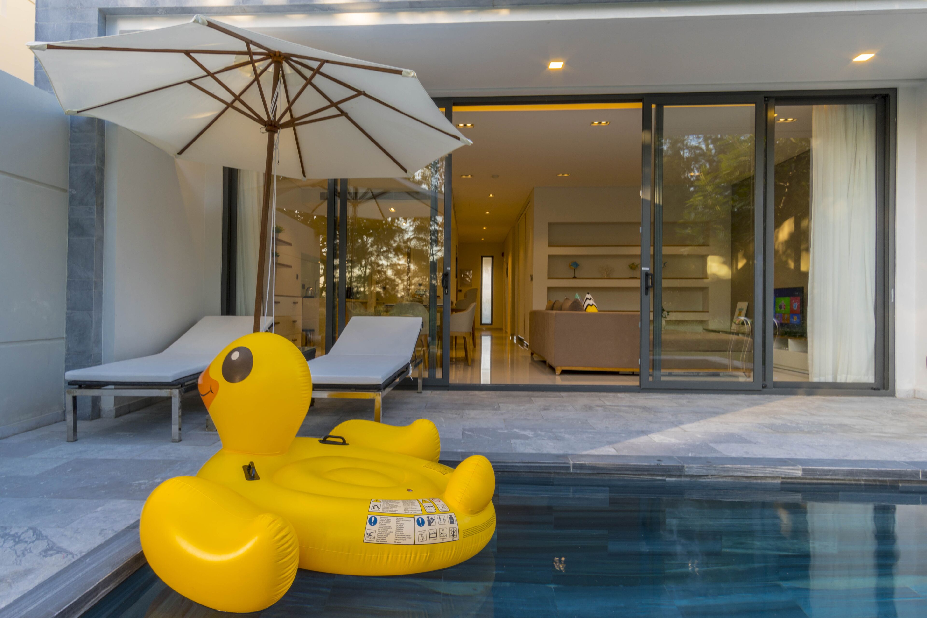A swimming pool with a yellow inflatable duck, a lounge chair, and an umbrella.