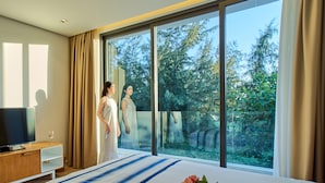 Ein modernes Hotelzimmer mit einem großen Bett, einem Fernseher und Blick auf Bäume durch das Fenster.