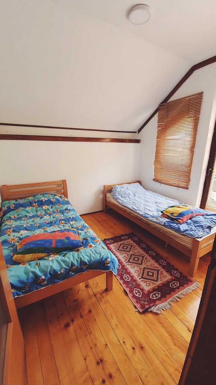 Een kamer met twee houten bedden, een kamerkleed met dessin en een raam met zonwering.
