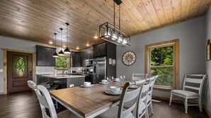 Een moderne keuken met houten plafond, roestvrijstalen apparatuur en een eethoek met witte stoelen en een houten tafel.