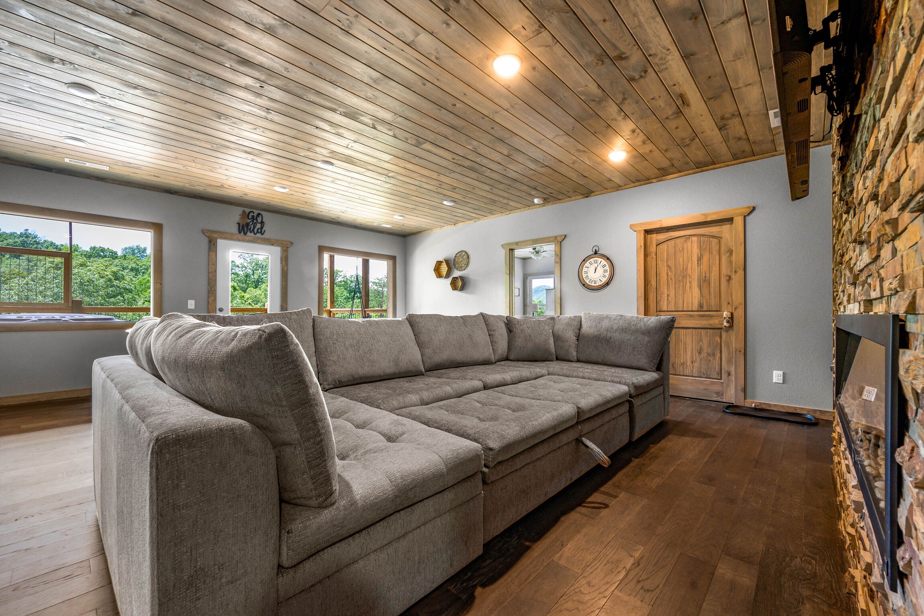 A modern living room with a large sectional sofa, wooden ceiling, stone wall, and a fireplace.