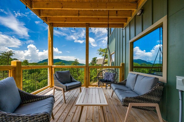 A wooden deck with wicker furniture and a view of a mountainous landscape.