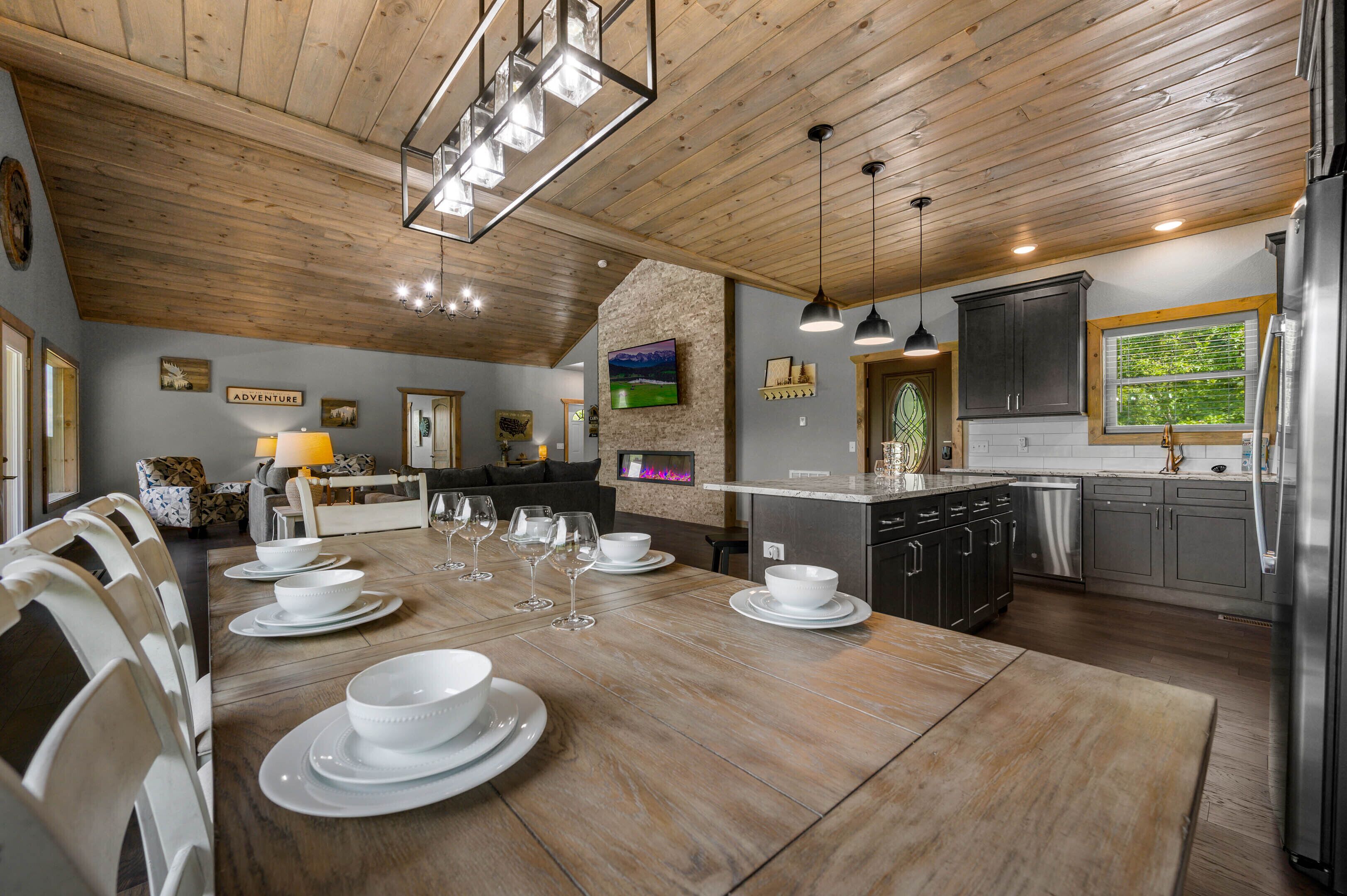 Un comedor amplio con una mesa de madera dispuesta para una comida, una cocina con electrodomésticos modernos y una zona de estar acogedora con chimenea.