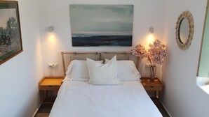 A bedroom with a bed, two bedside tables, a nightstand, a painting, a mirror, and a vase with flowers. - Villa Meli (Mykonos)