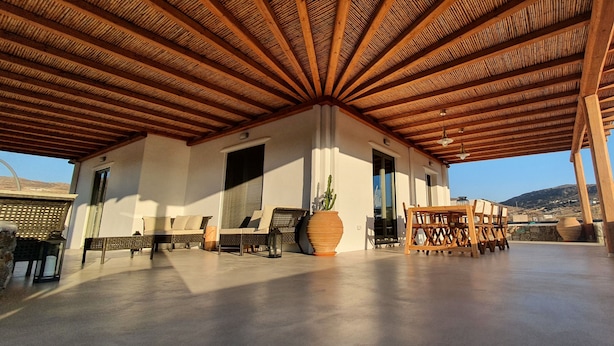 A covered outdoor area with a wooden ceiling, seating, and a large potted plant. - Villa Meli (Mykonos)