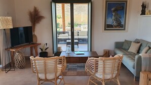 A living room with a television, wicker chairs, a sofa, and a painting of a statue. - Villa Meli (Mykonos)