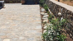 A stone pathway leading to a small stone building with a door and window, surrounded by plants and a stone wall. - Villa Meli (Mykonos)