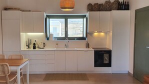 A compact kitchen with white cabinets, a dining table with chairs, a window with a view, and a built-in dishwasher. - Villa Meli (Mykonos)