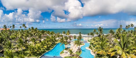 A resort with a large swimming pool, palm trees, and a view of the ocean.