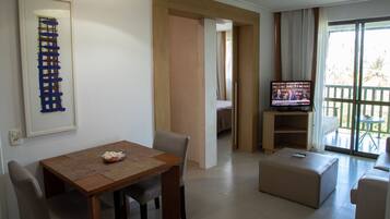 A living room with a wooden dining table, a sofa, a TV, and a balcony with a view.