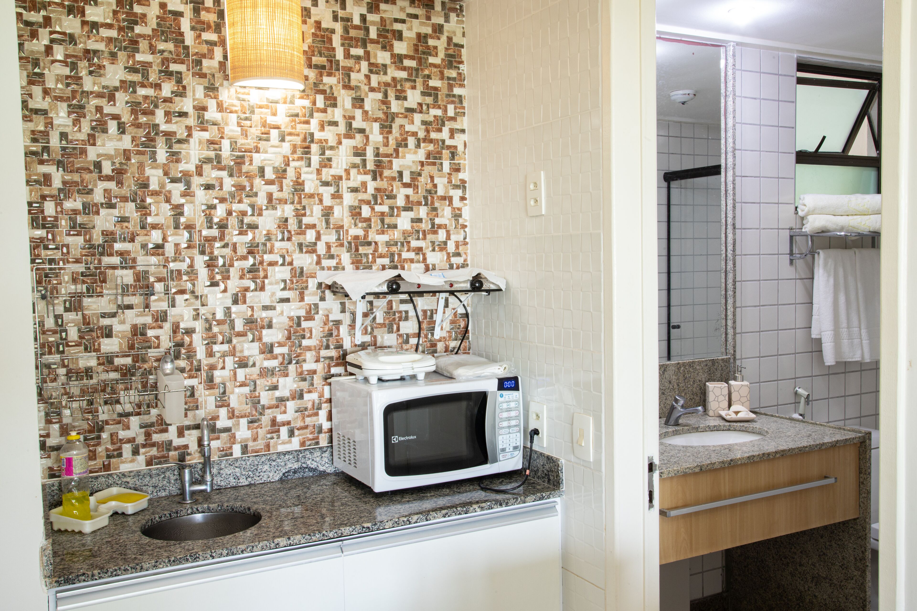 Un bagno con rivestimento in piastrelle, un lavandino, uno specchio e un forno a microonde sul ripiano.