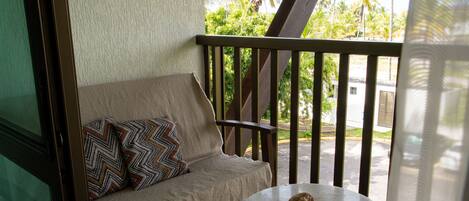 A balcony with a wooden railing, a beige sofa with patterned cushions, and a small round table with a rock on it.