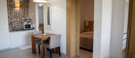 A compact hotel room with a kitchenette, a dining area, and a bed.