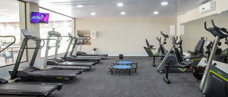 Un gimnasio con cintas de correr, elípticas y una bicicleta estática.
